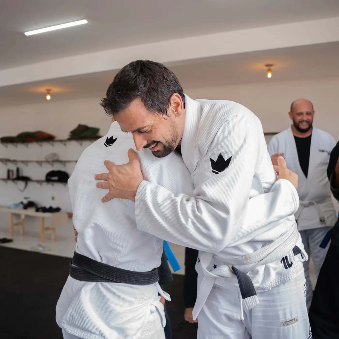Aluno adulto de kimono branco sorrindo durante o treino com um colega