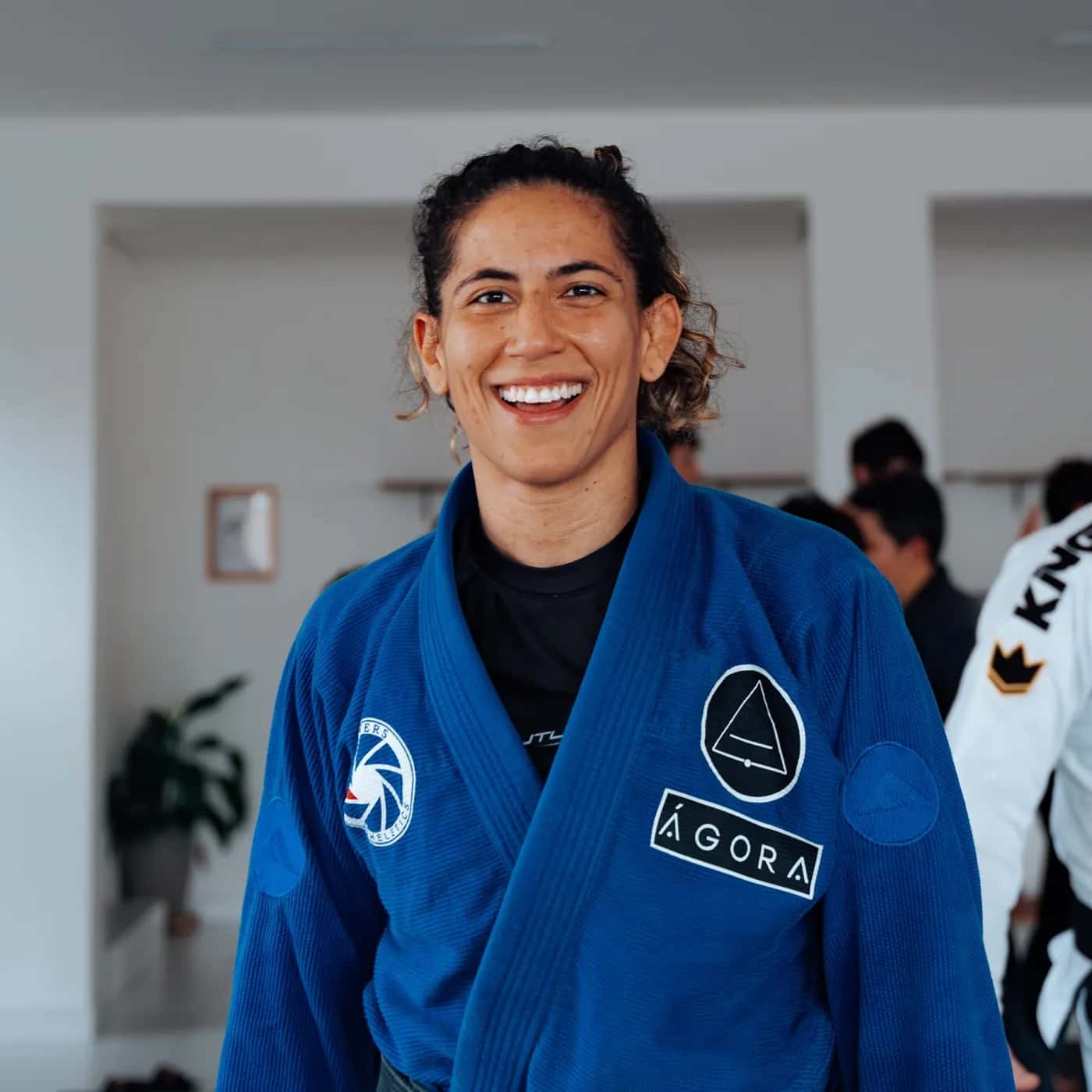 Professora da ÁGORA de kimono azul, sorrindo no tatame durante a aula